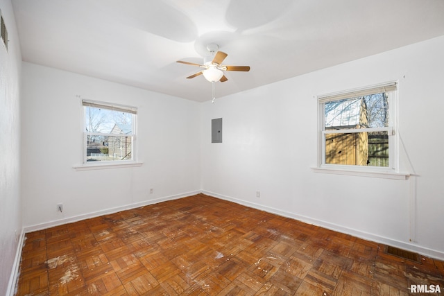 empty room with ceiling fan, plenty of natural light, electric panel, and dark parquet flooring