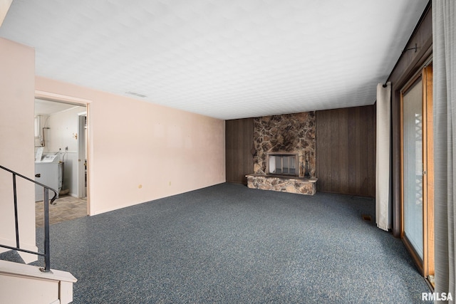 unfurnished living room featuring wooden walls, a stone fireplace, washer / clothes dryer, and carpet floors