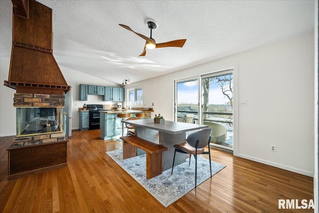 dining area featuring sink, hardwood / wood-style flooring, ceiling fan, a multi sided fireplace, and a textured ceiling