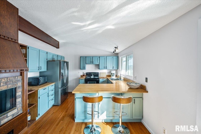 kitchen featuring blue cabinetry, black appliances, kitchen peninsula, and a kitchen bar