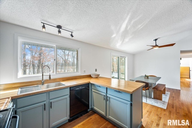 kitchen with wood counters, dishwasher, sink, kitchen peninsula, and light hardwood / wood-style flooring