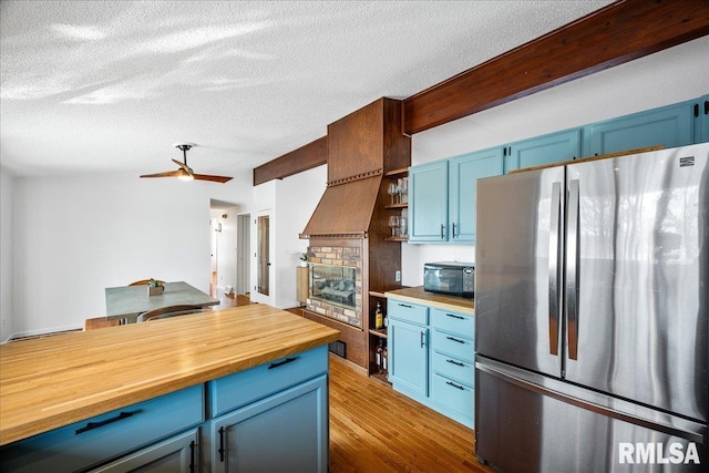 kitchen featuring blue cabinetry, dark wood-type flooring, stainless steel fridge, and wood counters