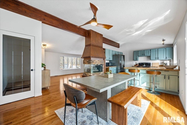 kitchen with refrigerator, beamed ceiling, a kitchen breakfast bar, black electric range, and light hardwood / wood-style flooring