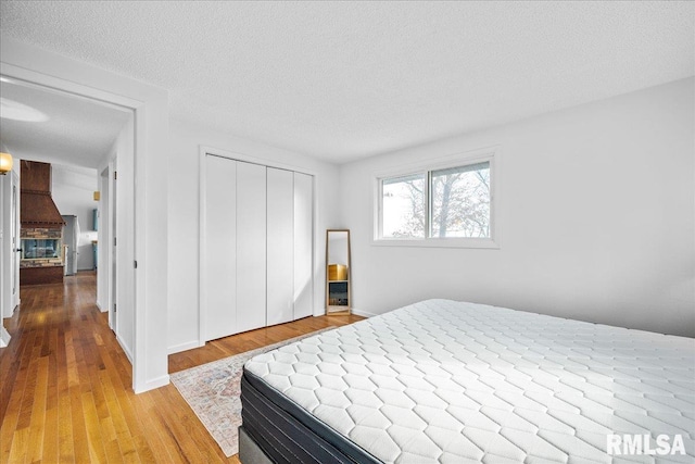 bedroom featuring a brick fireplace, a closet, a textured ceiling, and light wood-type flooring