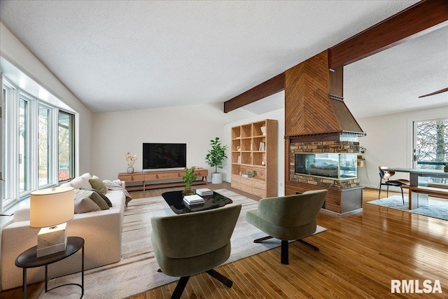 living room with wood-type flooring, a brick fireplace, a healthy amount of sunlight, and a textured ceiling