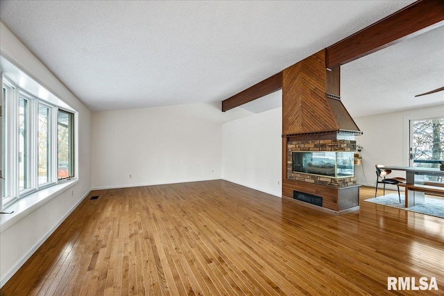 unfurnished living room featuring vaulted ceiling with beams, light hardwood / wood-style flooring, a textured ceiling, and a multi sided fireplace