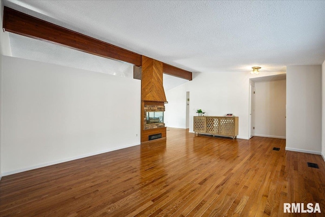 unfurnished living room with lofted ceiling with beams, hardwood / wood-style flooring, a textured ceiling, and a fireplace