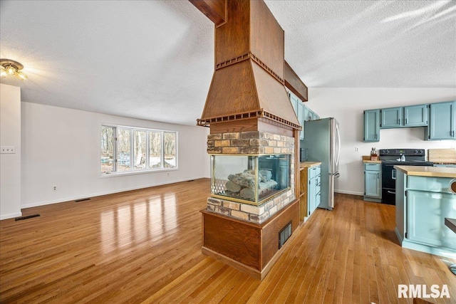 kitchen featuring a fireplace, stainless steel fridge, a textured ceiling, light wood-type flooring, and black / electric stove