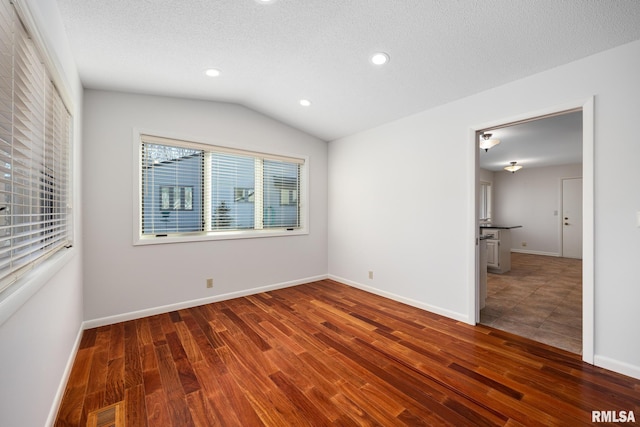 unfurnished room featuring dark hardwood / wood-style flooring, lofted ceiling, and a textured ceiling