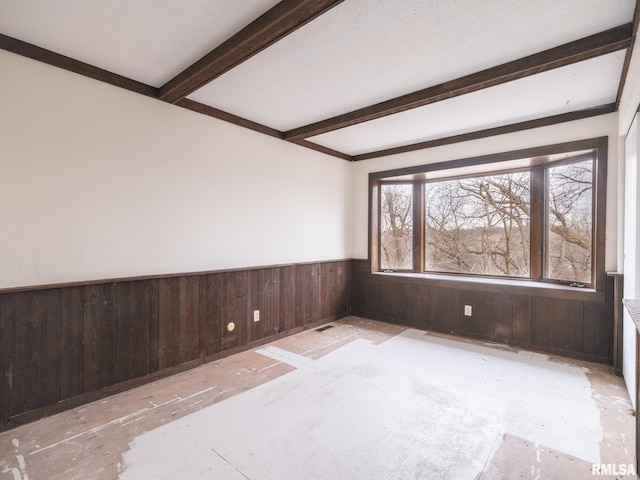 unfurnished room featuring beam ceiling and wood walls