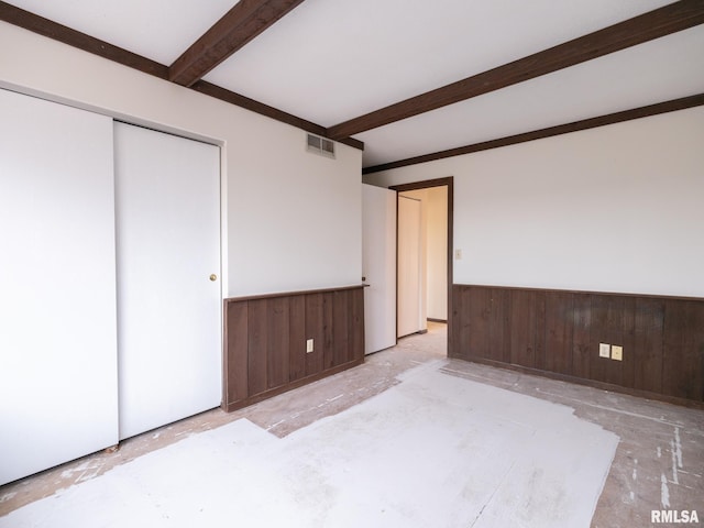 unfurnished bedroom featuring a closet, wooden walls, and beam ceiling