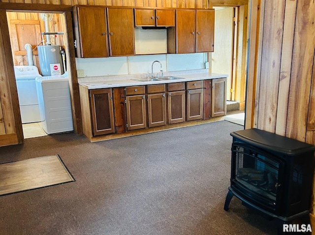 kitchen with sink, dark colored carpet, a wood stove, independent washer and dryer, and water heater