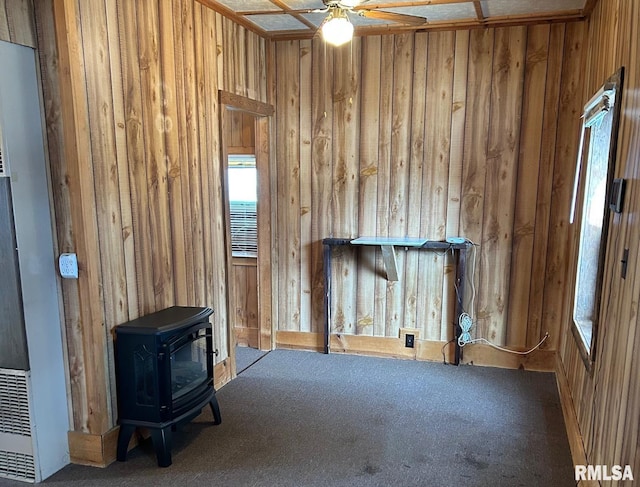 misc room with a wood stove, wooden walls, ceiling fan, and carpet flooring