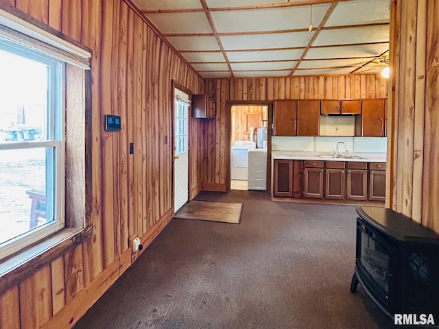 kitchen featuring dark carpet, sink, washing machine and dryer, and a wood stove