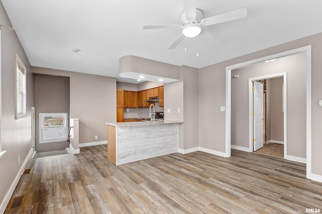 kitchen with ceiling fan, kitchen peninsula, sink, and light hardwood / wood-style flooring