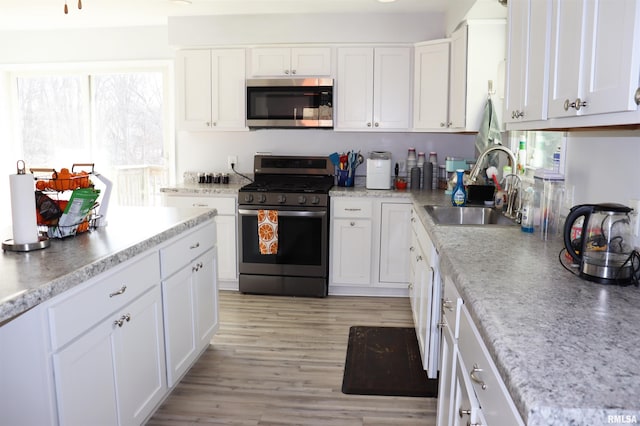 kitchen with white cabinets, light hardwood / wood-style floors, appliances with stainless steel finishes, and sink