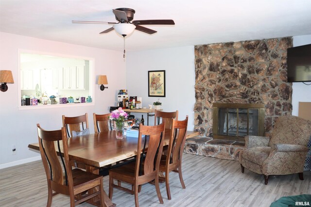 dining area featuring ceiling fan, a stone fireplace, and light hardwood / wood-style floors