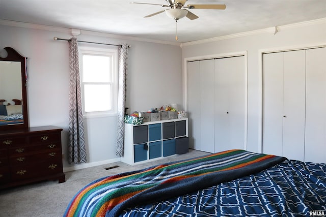 bedroom featuring ceiling fan, crown molding, light colored carpet, and two closets