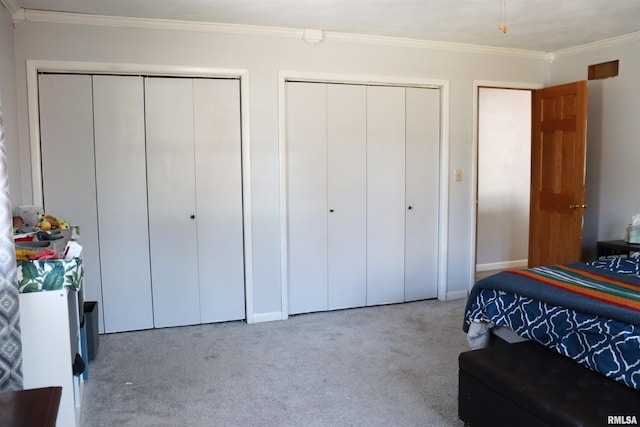 bedroom with crown molding, light colored carpet, and multiple closets