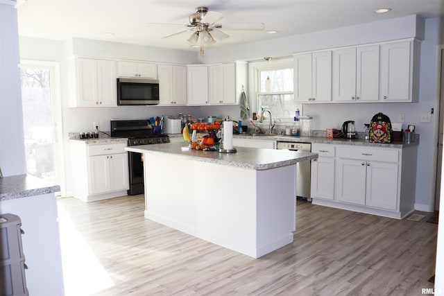 kitchen with appliances with stainless steel finishes, white cabinets, a center island, sink, and light wood-type flooring