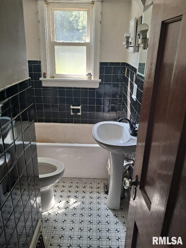 bathroom with tile walls, a washtub, tile patterned floors, and toilet