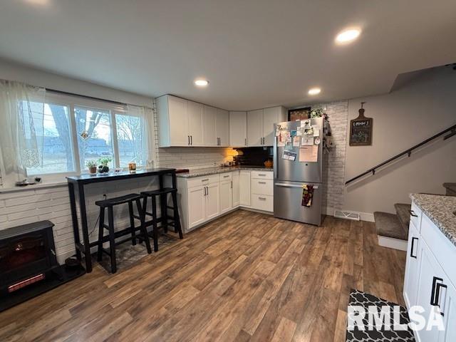 kitchen with stainless steel fridge, white cabinetry, dark hardwood / wood-style floors, tasteful backsplash, and light stone countertops