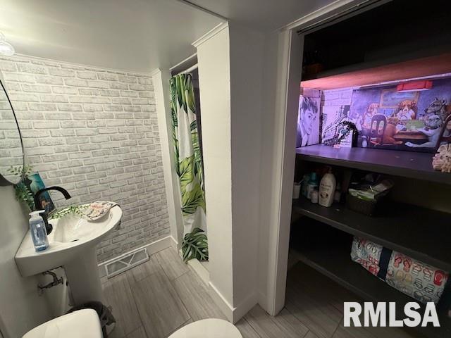 bathroom with a shower with curtain, toilet, and brick wall