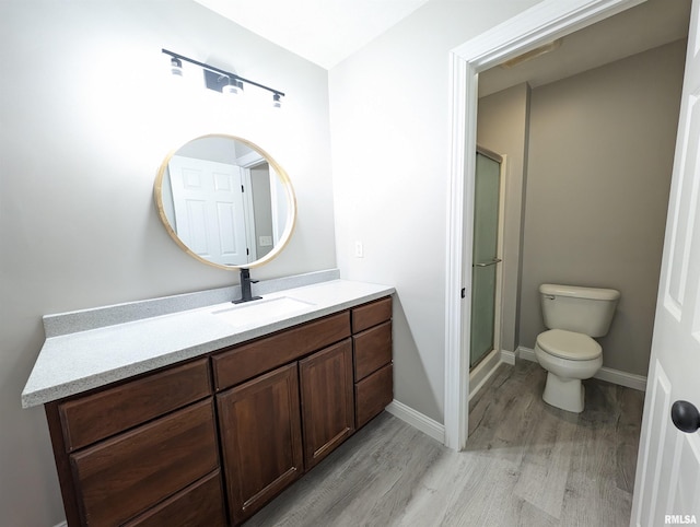 full bath featuring toilet, wood finished floors, vanity, baseboards, and a shower stall