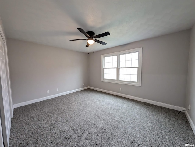 empty room with dark carpet, a ceiling fan, and baseboards