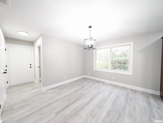 empty room with a notable chandelier and light wood-type flooring