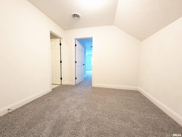 carpeted empty room featuring visible vents, vaulted ceiling, and baseboards