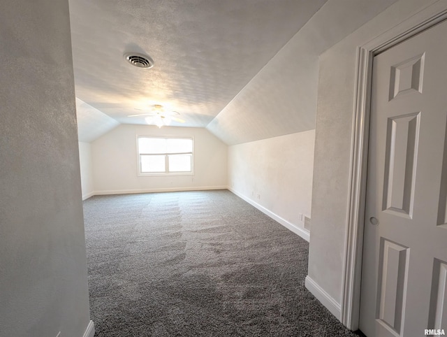 additional living space with a textured ceiling, carpet floors, visible vents, baseboards, and vaulted ceiling