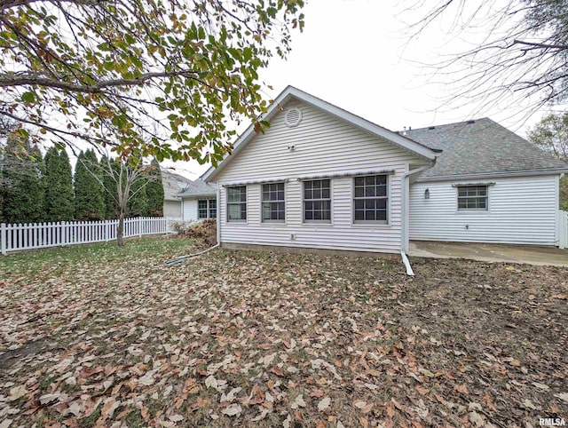 rear view of house featuring a shingled roof, fence, and a patio