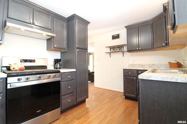 kitchen with sink, gas range, dark brown cabinets, light hardwood / wood-style flooring, and brick wall