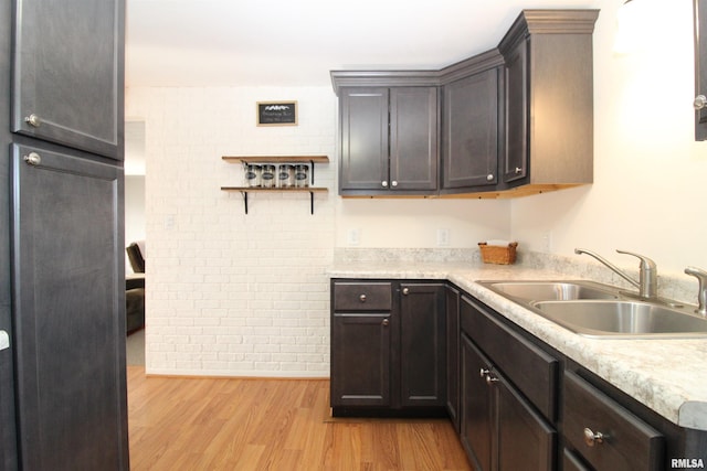 kitchen with sink, dark brown cabinets, brick wall, and light wood-type flooring