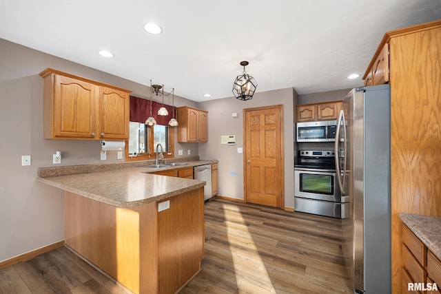 kitchen with dark wood-type flooring, sink, hanging light fixtures, kitchen peninsula, and stainless steel appliances