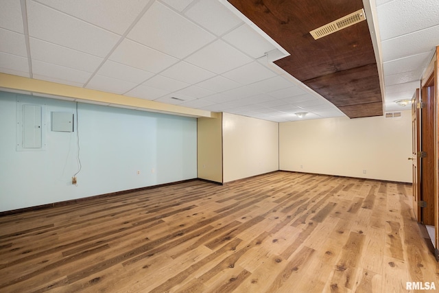 basement with a paneled ceiling, electric panel, and light wood-type flooring