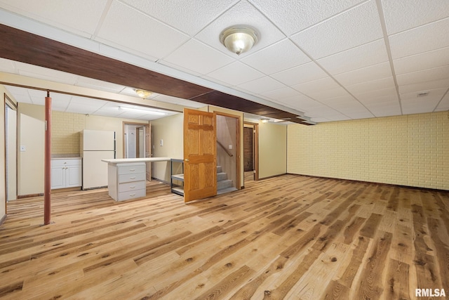 basement featuring brick wall, white fridge, a drop ceiling, and light hardwood / wood-style floors