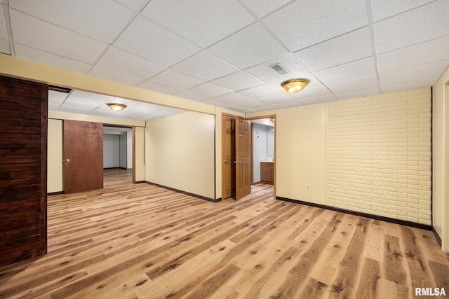 interior space with brick wall, a paneled ceiling, and light hardwood / wood-style floors