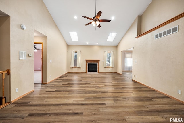 unfurnished living room featuring ceiling fan, dark wood-type flooring, high vaulted ceiling, and a skylight