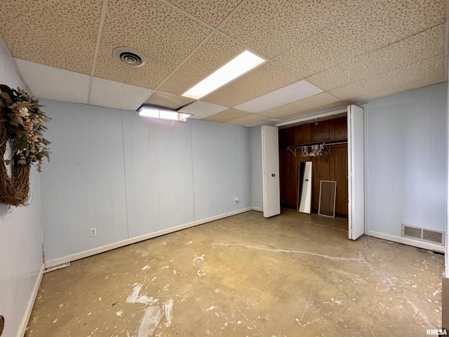 interior space with concrete flooring, a drop ceiling, wooden walls, and a closet