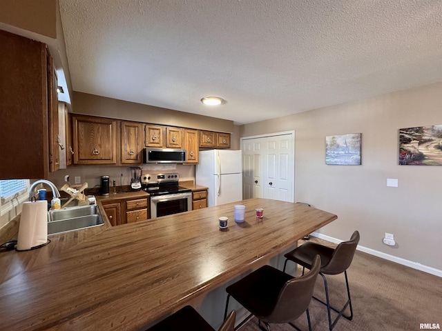 kitchen featuring sink, dark colored carpet, a textured ceiling, kitchen peninsula, and stainless steel appliances