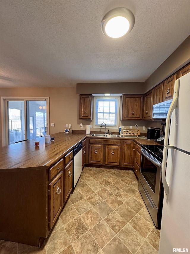 kitchen featuring sink, appliances with stainless steel finishes, butcher block counters, a textured ceiling, and kitchen peninsula