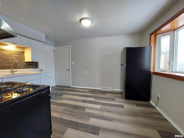 kitchen featuring sink, stainless steel refrigerator, black gas range, white cabinets, and dark hardwood / wood-style flooring