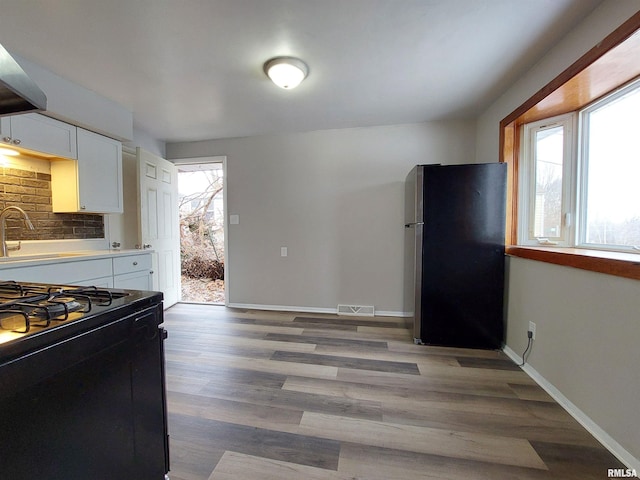 kitchen with sink, hardwood / wood-style flooring, stainless steel refrigerator, white cabinetry, and gas stove