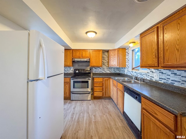 kitchen with under cabinet range hood, white appliances, a sink, brown cabinets, and light wood finished floors