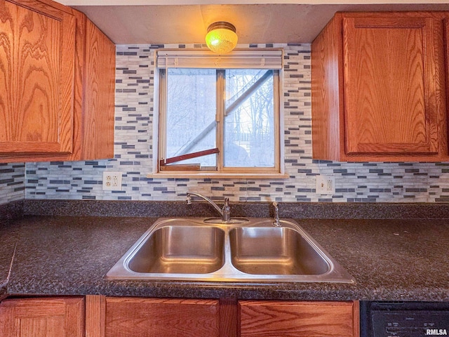 kitchen with black dishwasher, brown cabinetry, dark countertops, and a sink