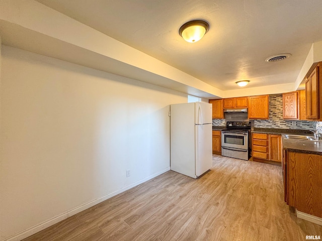 kitchen with tasteful backsplash, dark countertops, freestanding refrigerator, under cabinet range hood, and stainless steel range with electric stovetop