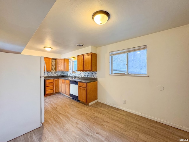 kitchen featuring light wood-type flooring, dishwasher, white fridge, a healthy amount of sunlight, and backsplash