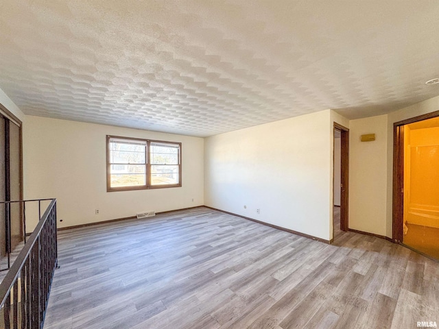 unfurnished room featuring baseboards, light wood-style flooring, visible vents, and a textured ceiling